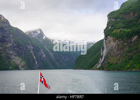 Sieben Schwestern Wasserfall des Berges gesehen von einem Auto Fähre Schiff mit einer norwegischen Flagge auf dem Geirangerfjord, Geiranger, Norwegen fallen. Stockfoto