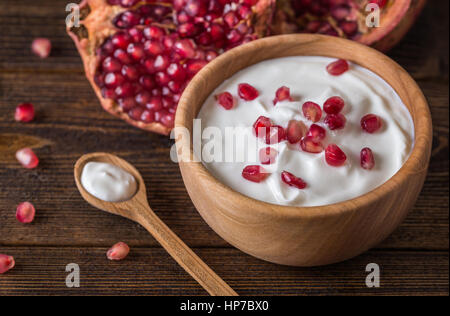 Joghurt mit Granatäpfeln in Holzschale auf rustikalen Tisch. Stockfoto