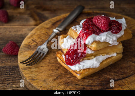 Belgische Waffeln mit Himbeeren und Sahne auf rustikalen Tisch. Stockfoto