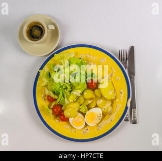 Draufsicht auf Salat mit Kartoffeln, Tomaten und Eiern, gechipt auf ein gelbes Schild, schwarzen Kaffee in einer Schale, vegetarisches Gericht Stockfoto