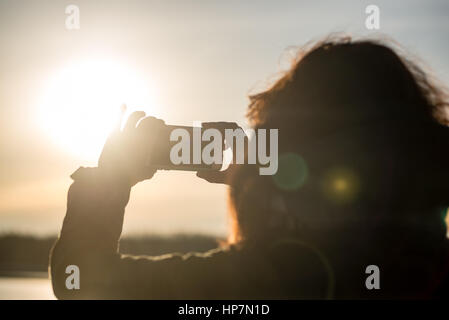 junge Frau, die Sonne mit dem Handy zu fotografieren. Menschen, die gefrorenen Strand im Winter kalt genießen. Wandern und entspannen Stockfoto