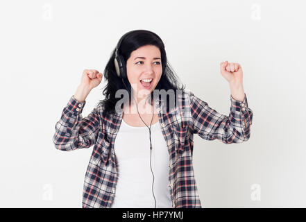 Junge Frau in einem großen Kopfhörer singt sein Lieblingslied und Tanz gegen eine weiße Wand Stockfoto