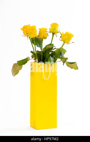 Gelbe Rosen in einer gelben Papiertüte isoliert auf weißem Hintergrund. Stockfoto