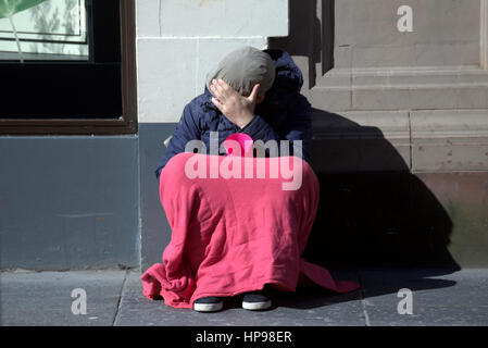 Gesicht versteckt intelligenter junger Mann auf Glasgow Straße Bettler betteln um Geld betteln mit Schale rosa Decke lässige Kleidung Farbe Vorderansicht voller Länge UK Stockfoto