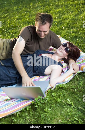 Model Release, Junges Paar so Mit Laptop Auf Einer Decke in der Wiese - paar mit Laptop in der Wiese liegend Stockfoto