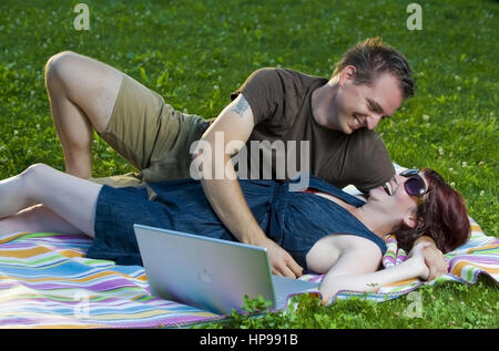 Model Release, Junges Paar so Mit Laptop Auf Einer Decke in der Wiese - paar mit Laptop in der Wiese liegend Stockfoto