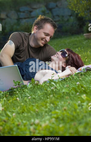 Model Release, Junges Paar so Mit Laptop Auf Einer Decke in der Wiese - paar mit Laptop in der Wiese liegend Stockfoto