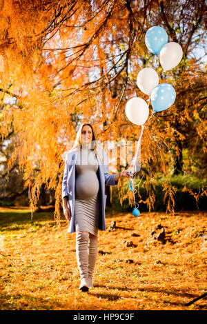 Junge schwangere Frau geht im Herbst Park mit Luftballons in der hand Stockfoto