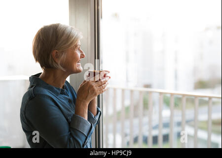 Ältere Frau am Fenster hält eine Tasse Kaffee Stockfoto