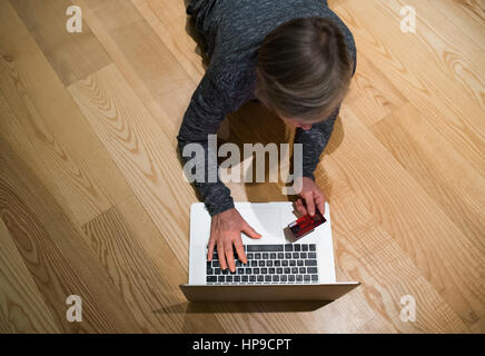 Ältere Frau mit Laptop auf dem Boden Online-shopping Stockfoto