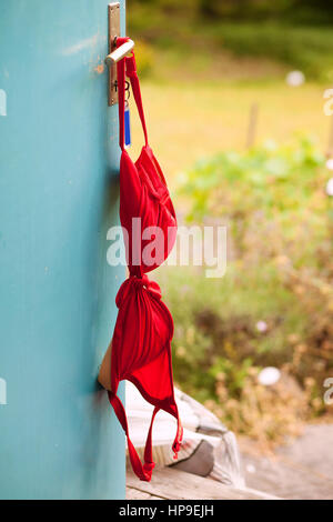 Roter Bikini-BH hängen an einem Türgriff in einer Hütte. Stockfoto