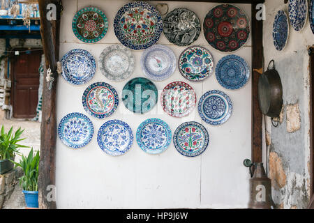 Weißer Wand dekoriert mit vielen keramischen Platten in blau und türkis-Tönen mit Pflanzen in Töpfen auf der linken Seite und Eisen Tablett hangin an Wand auf der rechten Seite Stockfoto