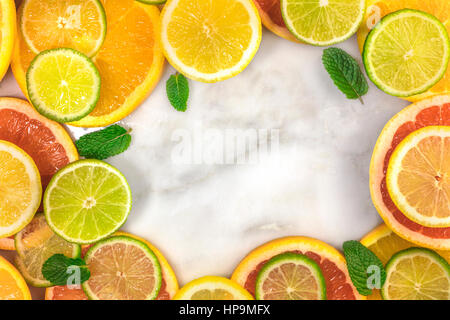 Einen lebendigen Rahmen, bestehend aus saftigen Zitrusfrüchten, auf eine weiße Marmor Textur mit Textfreiraum. Grapefruit, Limone, Zitrone und Orange Scheiben mit Minze Stockfoto