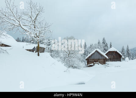 Holzhäuser in Schneeverwehungen auf der Piste im Winter ukrainischen Karpaten bei bewölktem Wetter. Stockfoto