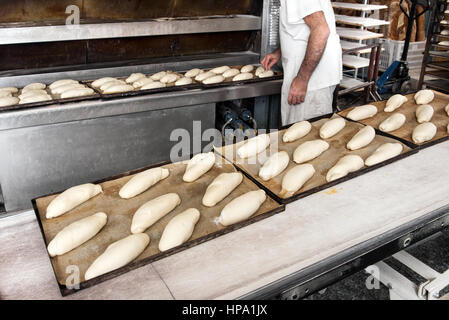 Inkognito männlichen Bäcker in weißem Hemd, die Herstellung von Brot, einige Töpfe mit Teiglinge kochbereit lange Brote auf den Tischen der Bäckerei Stockfoto