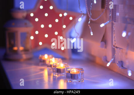 Feier-Dekoration für den Valentinstag. Glänzende Kerzen am Abend. Unscharfe Lichter im Hintergrund. Kerzen auf der Fensterbank. Stockfoto