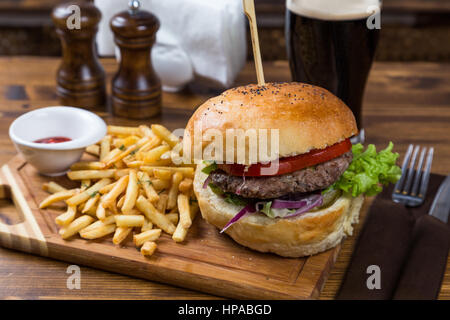 Hot Burger serviert auf Holzbrett mit dunklem Bier im restaurant Stockfoto