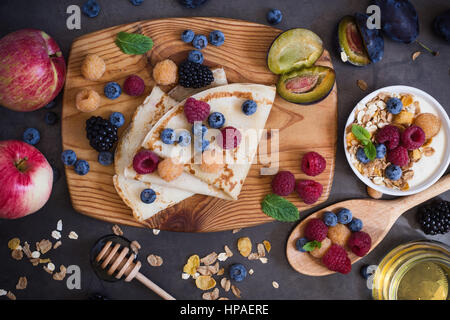 Gesundes Frühstück-Müsli und Crepes mit frischen Beeren und Früchte auf rustikalem Holzbrett, Ansicht von oben Stockfoto