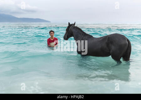 Gili Trawangan, Indonesien - 25. Januar 2017: Mann mit Pferd im Meer vor dem Hintergrund der bewölkten Himmel und Berge. Redaktionelle Fotos. Horizontale. Stockfoto