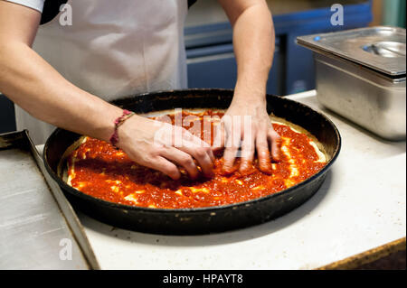 Nahaufnahme der männlichen Chef Hände arrangieren Zutaten auf der Pizza vor dem Backen in tiefe runde Pfanne Stockfoto