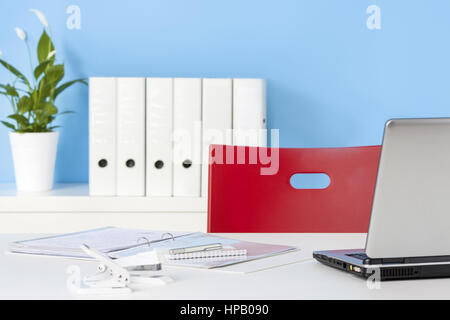 Schreibtisch mit rotem Stuhl vor blauer Wand Stockfoto