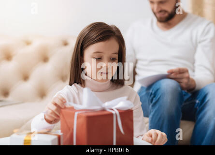 Geschenk für meine Mutter. Entzückende süße niedliche Mädchen am Tisch sitzen und unter einer Geschenkbox während der Vorbereitung auf ihre Mutter zu begrüßen Stockfoto