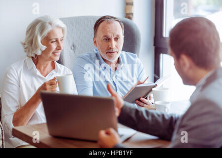 Es gibt verschiedene Möglichkeiten. Angenehm erfreut gealterten paar im Café sitzen und Treffen mit Versicherungs-Agent während des Gesprächs Stockfoto