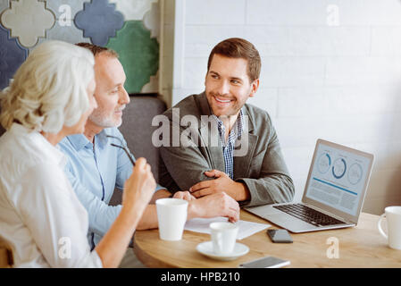 Schauen Sie sich die Daten. Angenehme insurance Manager im Gespräch mit positiven gealterten paar beim Sitzen im café Stockfoto