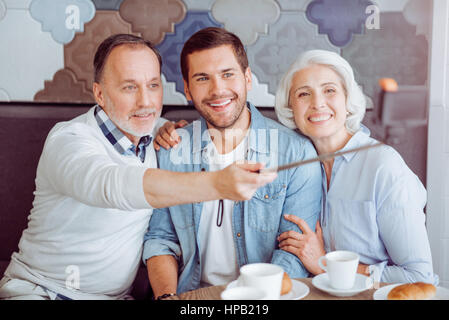 Fangen Sie den Augenblick. Positiv im Alter von paar und Thir Enkel machen Selfies und Mittagessen im Café sitzend Stockfoto