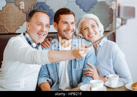 Genießen Sie den Augenblick. Angenehme liebende Paar und ihre Enkel im Café sitzen und Selfies zu machen, während dem Mittagessen im Alter von Stockfoto