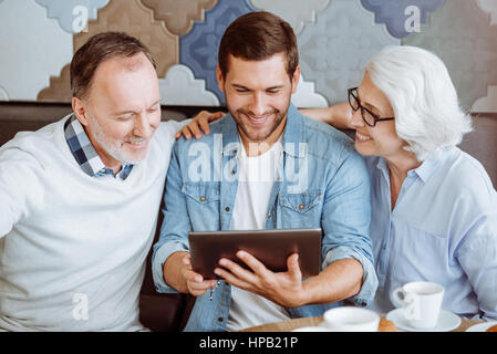 In der Metwork. Positiv erfreut älteres Paar und ihre Enkel im Café sitzen und mit tablet-beim Ausruhen zusammen Stockfoto