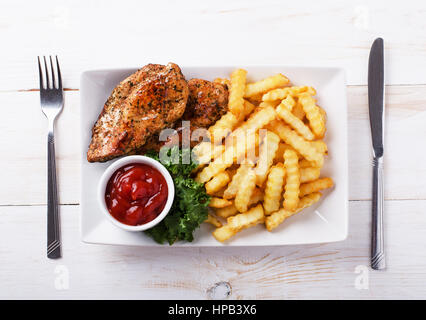 Brathähnchen auf einem Teller mit Pommes und Ketchup auf weißen Tisch Stockfoto