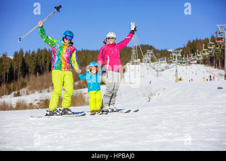 Fröhliche Familie mit drei stehend auf Skipiste, Eltern, die Hände mit Ski-Stöcke Stockfoto