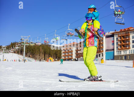 Vater müde Sohn im Ski-Outfit auf Schultern tragen. Stehend auf Skipiste mit Sesselliften. Stockfoto