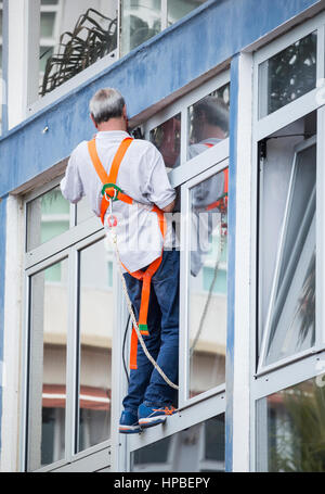 Mann mit Elektrowerkzeug balancieren prekär auf Fenstersims. Stockfoto
