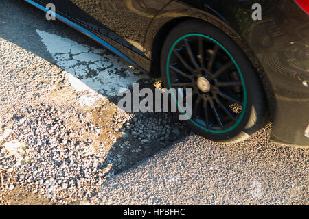 Auto-Rad über ein Schlagloch fahren / Schlagloch / Löcher / Schlaglöcher wo die Straße / Straße trifft eine Bremsschwelle / Speedbump, um den Verkehr zu verlangsamen. VEREINIGTES KÖNIGREICH. Stockfoto