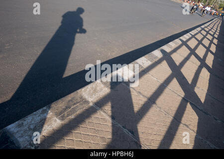 Indischer Mann, ein Bild von seinem eigenen Schatten stehend auf einem Bürgersteig neben Geländer in Hyderabad, Indien Stockfoto