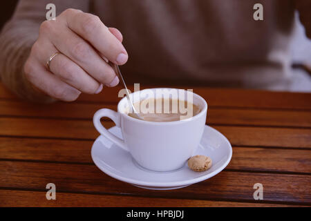 Detail des Mannes Hand hält einen Löffel Rühren eine Tasse Espresso, Pausenzeit, im freien Stockfoto