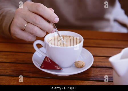 Detail des Mannes Hand hält einen Löffel Rühren eine Tasse Espresso, Pausenzeit, im freien Stockfoto