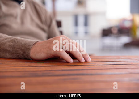 Hand des jungen Mannes mit einem goldenen Hochzeit Ring auf Holztisch, der Hintergrund jedoch unscharf Stockfoto