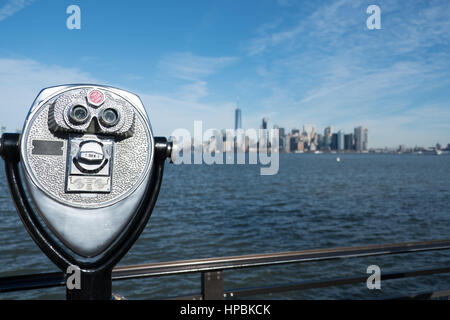 Turm-Viewer Fernglas auf einem drehbaren Standfuß neben einem Geländer am Rande von Liberty Island, New York City.  Blick auf Lower Manhattan und New York Harbor Stockfoto