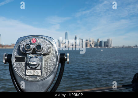 Ragen Sie Viewer-Ferngläser, die aussehen wie ein Gesicht auf Liberty Island mit New York Hafen und die Skyline von Manhattan in der Ferne.  Blauer Himmel, hell Stockfoto