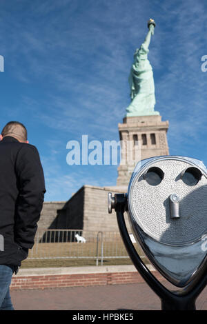 Der Mensch geht an der Freiheitsstatue vorbei ein Turmbetrachter auf Liberty Island. Schöner sonniger Tag mit blauem Himmel und Wolken. Seitenansicht, Freiheitsstatue. Stockfoto