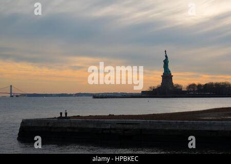 Silhouette der Statue of Liberty bei Sonnenuntergang im Hafen von New York.  Abend-Ansätze als die Sonne untergeht auf die Statue of Liberty.  Dramatische Wolken, Ansicht Stockfoto