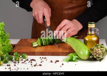 Koch schneiden lange grüne Gurke auf ein Holzbrett unter grünen vehetanles Stockfoto