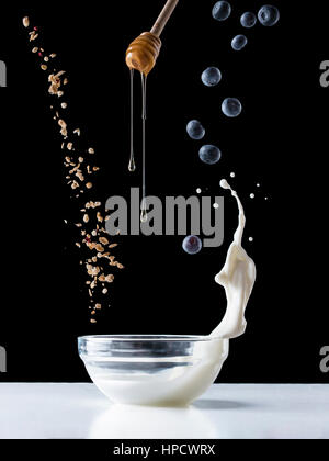 Fallende Müsli mit Milch Spritzen, Heidelbeeren und Honig fließt vom Wagen fallen. Gesundes Frühstückszutaten. Fliegendes Essen Stockfoto