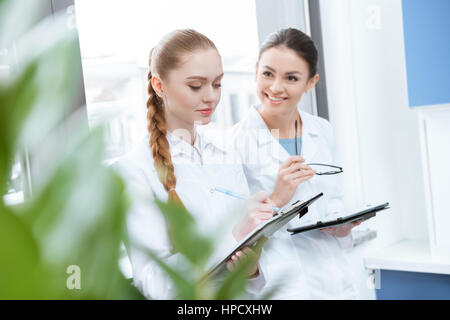 Junge Wissenschaftlerinnen in weißen Kitteln mit Zwischenablage und digital-Tablette in lab Stockfoto