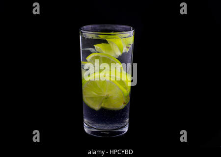 Scheiben von Kalk in Glas Wasser mit Kohlensäure auf schwarzem Hintergrund. Beliebt und lecker Sommer trinken, kalte Limonade. Ästhetische geschossen im Sommer trinken. Stockfoto