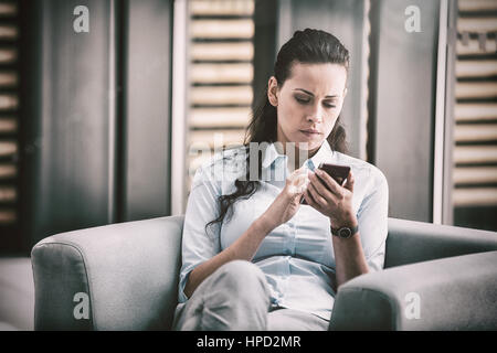 Geschäftsfrau sitzt auf Sessel und Handy Stockfoto