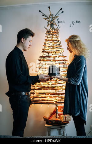 Mädchen gibt dem Mann einen Kuchen gegen eine weiße Wand Stockfoto